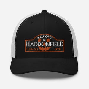 May include: Black and white trucker hat with a black and orange embroidered patch that says "Welcome to Haddonfield, Illinois 1978". The patch features a jack-o-lantern face.