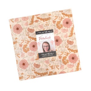 May include: A square piece of fabric featuring a floral pattern with muted pink flowers and golden-brown foliage on a cream background. A rectangular label is centered on the fabric, displaying the text moda Petalush by Kiley's Quilt Room.