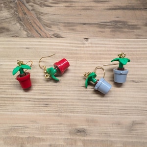 May include: Four pairs of earrings featuring miniature potted plants made from Lego pieces. Two pairs have red pots and two pairs have grey pots.