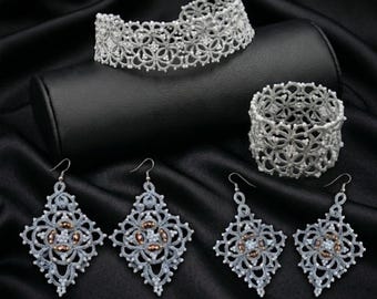 Puede incluir: Un conjunto de joyería compuesto por una gargantilla de encaje blanco, una pulsera de encaje ancha a juego y dos pares de pendientes de encaje en forma de rombo, con intrincados hilos blancos, cuentas pequeñas y detalles en color cobre.