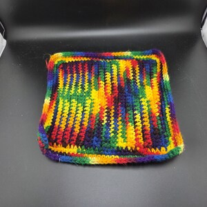 May include: A square, handmade crochet potholder in a vibrant rainbow of colors. The potholder features a striped pattern with red, orange, yellow, green, blue, and purple yarns. The edges are neatly finished, creating a durable and colorful kitchen accessory.