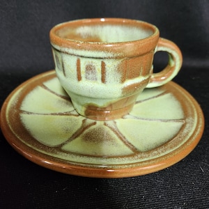 May include: A green and brown ceramic teacup and saucer set. The cup has a brown rim and a green and brown glaze. The saucer has a brown rim and a green and brown glaze with a decorative pattern.