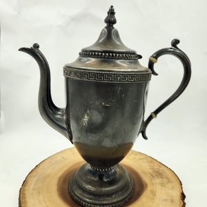 May include: A silver teapot with a decorative design around the top and a fluted base. The teapot has a spout and a handle.