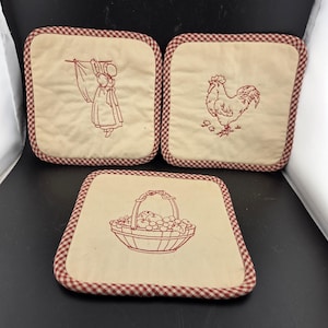 May include: Set of three square beige pot holders with red gingham trim. Each pot holder features a different embroidered design: a woman hanging laundry, a rooster with chicks, and a basket of fruit.