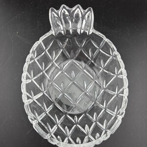 May include: Clear glass pineapple-shaped serving bowl. The bowl features a diamond pattern across its surface and a crown-like top. The bowl is designed to resemble a pineapple fruit and is suitable for serving snacks or small dishes.