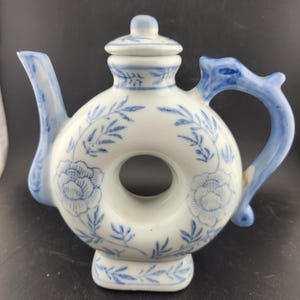 May include: A white ceramic teapot with a blue and white floral design. The teapot has a round body with a hole in the center and a dragon-shaped handle.