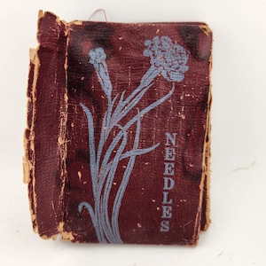 May include: A vintage red leather needle case with a blue floral design and the word "NEEDLES" printed on the front.