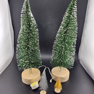 May include: Four artificial Christmas trees, two large green trees with white flocked tips, one small silver tree, and one small gold tree. All trees are on wooden bases.