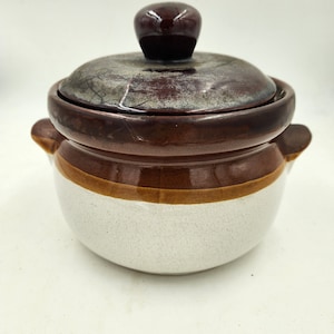 May include: A brown and white ceramic pot with a lid. The lid has a brown knob. The pot has a brown band around the middle.