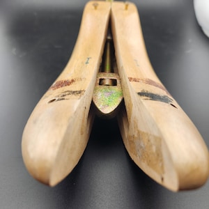 May include: Wooden shoe stretcher with a metal screw mechanism. The stretcher is open and the screw is visible. The stretcher is made of light brown wood.