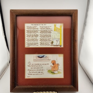 May include: A framed print with two panels. The top panel features text and an illustration of a bed and a pot. The bottom panel shows a baby on a potty with text. The frame is brown.