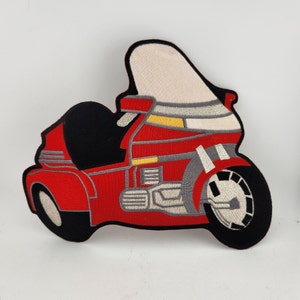 May include: Embroidered patch of a red motorcycle with black and gray accents. The motorcycle has a large windshield and detailed stitching on the wheels and body. The patch is designed to be ironed or sewn onto fabric.