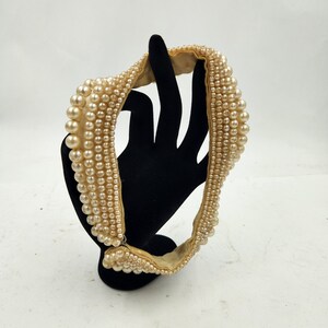 May include: A cream-colored faux pearl necklace with a satin ribbon backing. The necklace is displayed on a black velvet stand.