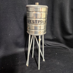 May include: A silver metal water tower model with the words "WEST POINT" printed on the side. The tower is mounted on a silver metal stand with four legs.