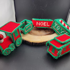 May include: A set of five Christmas train cars made of green and red felt with white accents. The cars are decorated with the words "NOEL" and "TOYS".
