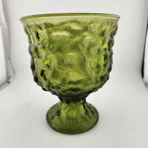 May include: A green glass vase with a textured surface and a pedestal base.