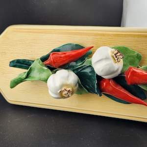 May include: A wooden cutting board with a decorative design of red chili peppers and white garlic cloves. The design is three-dimensional and appears to be made of ceramic.
