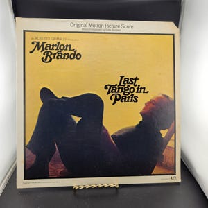 May include: A vintage vinyl record album cover for "Last Tango in Paris" featuring Marlon Brando. The cover has a yellow background with black text and a silhouette of a person. The album is an original motion picture score.