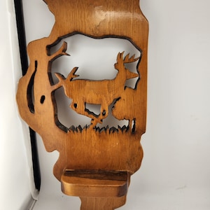 May include: A wooden wall shelf with a carved deer silhouette. The shelf is stained a dark brown color and has a small ledge for displaying items.