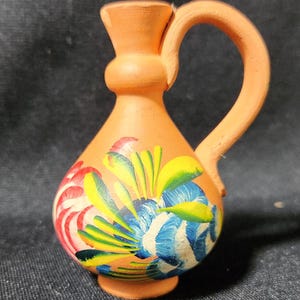 May include: A small terracotta pitcher with a handle, painted with colorful flowers in shades of red, yellow, blue, and green.
