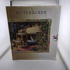 May include: A hardcover book titled Nutcracker by E.T.A. Hoffmann and illustrated by Roberto Innocenti. The cover features a detailed illustration of a child lying on a red cushion reading a book near a decorated Christmas tree and a wooden chair.