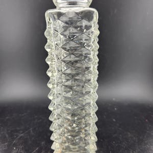 May include: A clear glass vase with a diamond-shaped pattern. The vase is tall and slender, with a wide mouth and a narrow base.