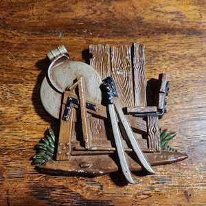 Puede incluir: Una decoración de pared de madera con una piedra de moler, una silla de madera y dos esquís. La piedra de moler está pintada de gris y tiene una correa de cuero marrón. La silla está pintada de marrón y tiene un respaldo pintado de blanco. Los esquís están pintados de blanco y tienen puntas negras.