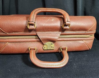 May include: A vintage brown leather suitcase with brass hardware and a zipper closure. The suitcase has two handles, one on the top and one on the side.