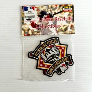 Könnte beinhalten: Ein Pittsburgh Pirates 1994 All-Star Game Patch. Der Patch ist schwarz, rot und goldfarben, mit den Worten "Pittsburgh Pirates" und "1994 All-Star Game" in weißer Schrift. Oberhalb des Patches befindet sich eine Baseball-Sammelkarte.