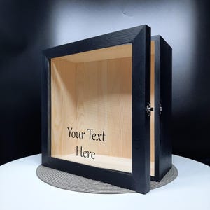 May include: Black wooden shadow box with a glass front and a hinged lid. The inside of the box is lined with natural wood. The box has a personalised inscription that reads "Your Text Here".