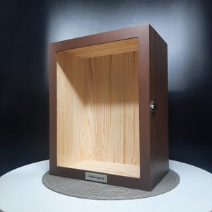 May include: A brown wooden box with a hinged lid and a metal latch. The inside of the box is lined with wood and has a small shelf. The box has a metal plaque on the front that reads "The Mommyfamily".