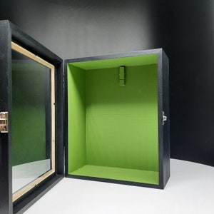 May include: A black wooden shadow box with a glass front and a green felt interior. The box has a hinged lid and a metal latch.