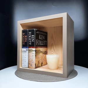 May include: A wooden shelf unit with three books by Ken Follett, "Fall of Giants", "World Without End", and "Edge of Eternity", and a white candle.