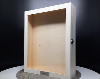 May include: White wooden shadow box with a glass front and a metal latch. The box has a small metal plate on the bottom with the text "The Almanac Family" engraved on it.