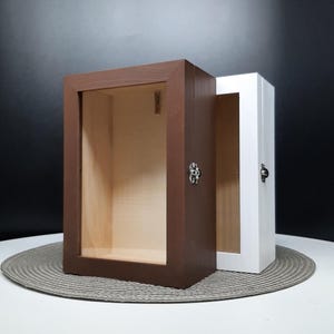 May include: Two wooden shadow boxes with glass fronts. One box is brown and the other is white. Both boxes have a small metal latch.