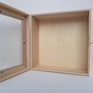 May include: Open wooden display box with a clear glass front. The box is made of light-colored wood and has a hinged door. The interior is a light tan color. The box is empty and ready for display.