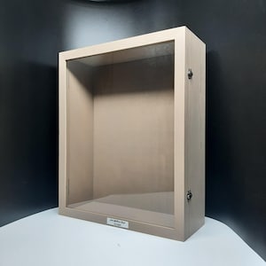 May include: A light brown wooden shadow box with a glass front and a silver label that reads "John Matthew Angel 6-8-2024".