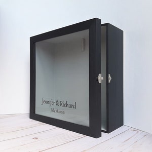 May include: Black wooden shadow box with a glass front. The box is open and has a personalized inscription that reads "Jennifer & Richard July 18, 2016".