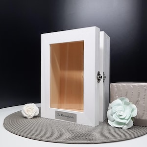 May include: White wooden box with a glass front and a hinged door. The box has a silver plaque with the text "The Momminfamily" on it.