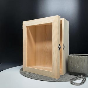 May include: A wooden shadow box with a hinged front and a natural wood finish. The box is open and the interior is visible.