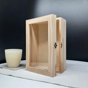 May include: A wooden display case with a glass front and a hinged door. The case is made of natural wood with a light brown finish. The case is empty and ready to be filled with your favorite items.