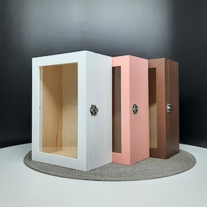 May include: Three wooden display boxes with clear glass fronts and metal catches. The boxes are white, pink, and brown.