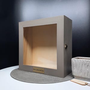 May include: A gray wooden shadow box with a glass front and a brass plaque that says "Your custom text here".