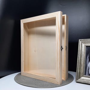 May include: A wooden shadow box with a clear glass front and a hinged door. The box is made of natural wood and has a simple, rustic design.