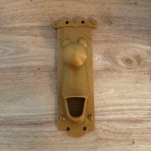 May include: A gold-coloured door handle shaped like a face with a large nose and open mouth. The handle is made of plastic and has a textured surface.