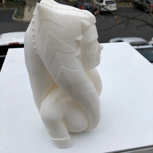 May include: White 3D printed bust of a female character with a detailed headpiece and a flowing robe. The bust is posed in profile, with the character's face turned slightly towards the viewer.