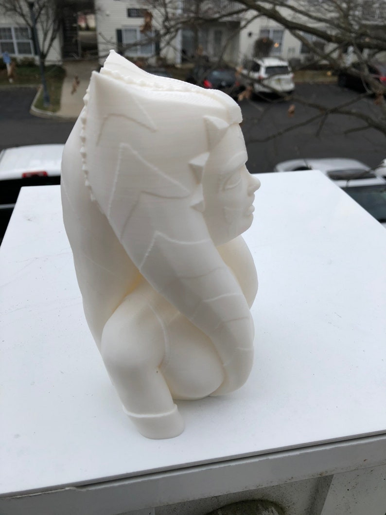 May include: White 3D printed bust of a female character with a detailed headpiece and a flowing robe. The bust is posed in profile, with the character's face turned slightly towards the viewer.