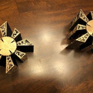 May include: Two gold and black metal puzzle boxes with intricate designs. The boxes are closed and have a starburst pattern on the top.