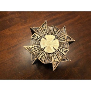 May include: A gold-colored metal puzzle box with intricate designs. The box is shaped like a star with multiple layers and a circular center.
