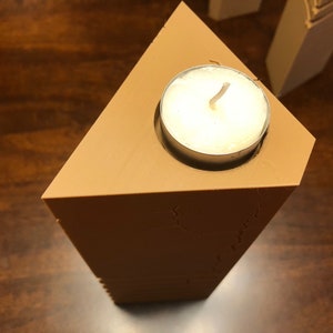 May include: A triangular wooden candle holder with a white tea light candle in the center.